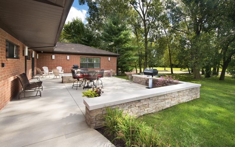 a patio with chairs and tables and a brick building with trees and grass